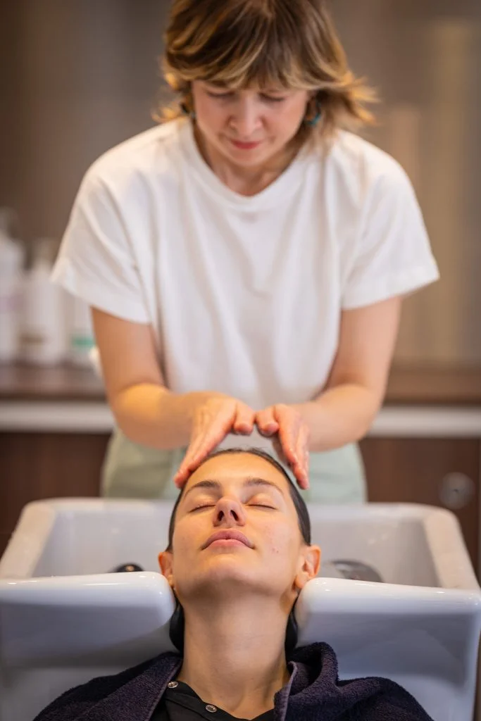 Coiffure femme où la femme se fait laver les cheveux; les doigt du coiffeur caresse les cheveux doucement. Cela se passe dans un salon de coiffure lumineux à paris 6
