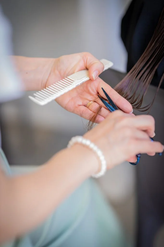 Coiffure femme réalisé à l'aide de ciseux japonais bleus. Nous voyons les deux mains de la coiffeuse tenant les ciseaux et un peigne nacré blanc