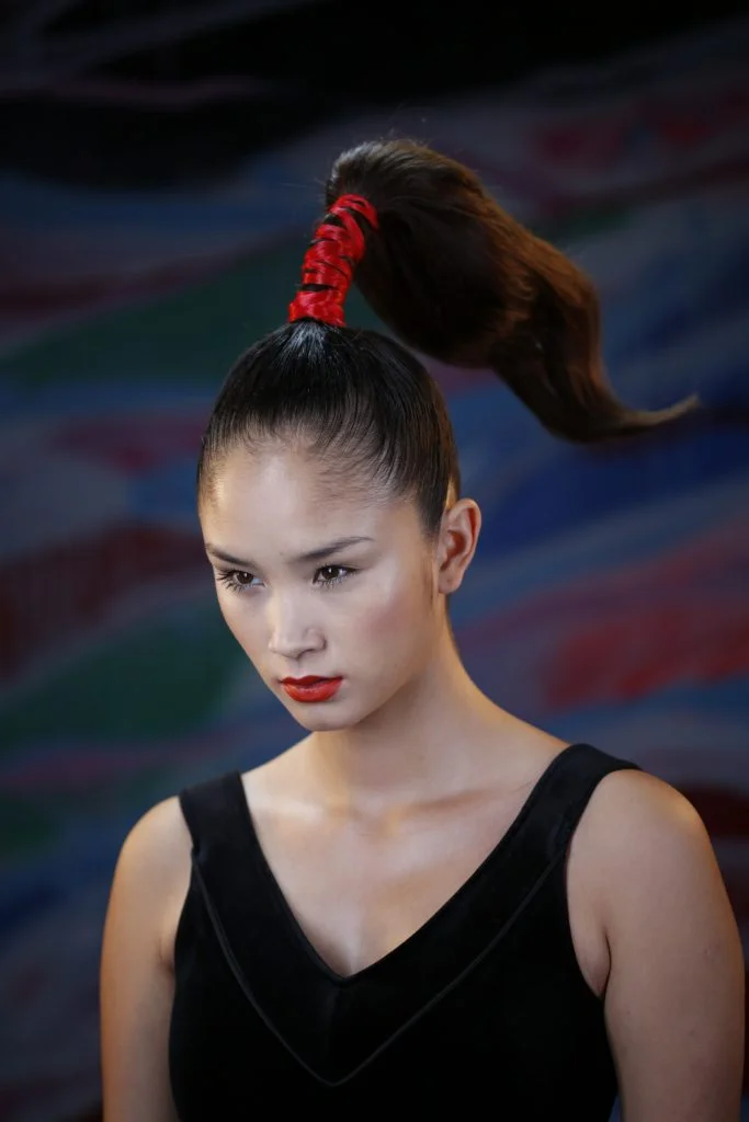 C'est une coiffure femme composée d'un chignon Japonais. Elle a des cheveux noire et une tresse rouge. Le fond est un fond de studio photos