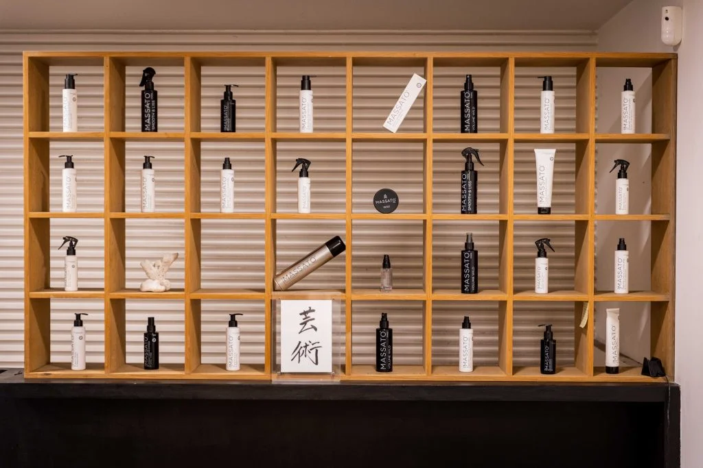 chez Massato coiffeur. Nous voyons des étagère carré en bois clair. Et à l'intérieur la décoration est assuré par des produit capillaire et ds tableau Japopnais.